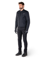 Männlicher Fahrer in der Alpinestars Clayton WR Jacke, schwarze Urban-Motorradjacke, Slim-Fit-Design mit gesteppten Schulterakzenten und mattem Finish, kombiniert mit schwarzer technischer Motorradhose und Handschuhen.