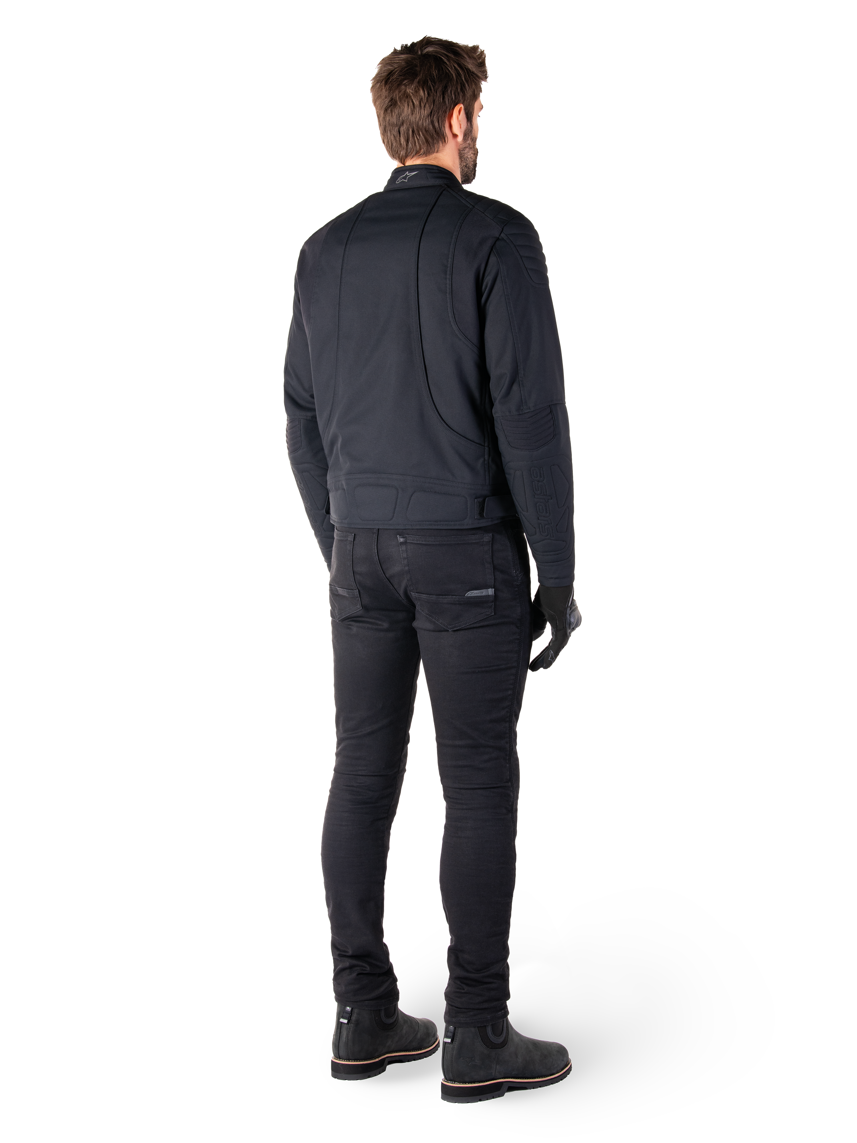 Rückansicht eines Fahrers in der schwarzen Alpinestars Clayton WR Jacke, mit gesteppten Paneelen an Ellbogen und Schultern, ergonomisch geschwungenen Nähten und reflektierenden Details am Kragen, kombiniert mit schwarzer Motorradhose und Stiefeln für einen urbanen Look.