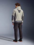 Männliches Model in der Rückansicht, trägt die Alpinestars Moblast Waterproof Jacke in Iron Gray Dark Sage, urbane Motorradjacke mit Kapuze, dunkelgrauen Seiteneinsätzen und verstärkten Ellbogen-Patches, kombiniert mit dunkler Motorradhose und schwarzen Sneakern, moderne minimalistische Ästhetik für den urbanen Pendelverkehr.