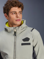 Alpinestars Moblast Wasserdichte Jacke, Iron Gray Dark Sage, Nahaufnahme eines männlichen Models, das die Jacke trägt, mit schwarzem Alpinestars-Logo und MO.ST.EQ.-Brustaufnähern, leuchtend gelbem Kapuzenfutter und einem modernen technischen Design.
