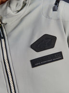 Alpinestars Moblast Wasserdichte Jacke, Iron Gray, Nahaufnahme der Brustaufnäher mit dem Alpinestars Logo und MO.ST.EQ. Moto Streetwear Equipment Branding, technisches Ripstop-Gewebe mit robustem Frontreißverschluss und Detail der Schultertasche.