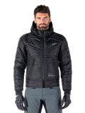 Alpinestars Mohobbs Waterproof Jacket, schwarze gepolsterte Bomber-Motorradjacke, gestepptes Polygewebe mit Frontreißverschluss und Reißverschlusstaschen, kleines weißes Logo auf der Brust, Modell trägt graue Hose und Handschuhe, urbanes Streetwear-Design für Stadtfahrten