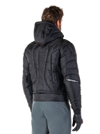 Alpinestars Mohobbs Wasserdichte Jacke, Schwarz, Rückansicht mit gesteppter wattierter Konstruktion, Kapuze, vertikaler Astars-Schriftzug auf dem Rücken und Alpinestars-Branding auf den Ärmeln, getragen mit grauer Hose und schwarzen Handschuhen.