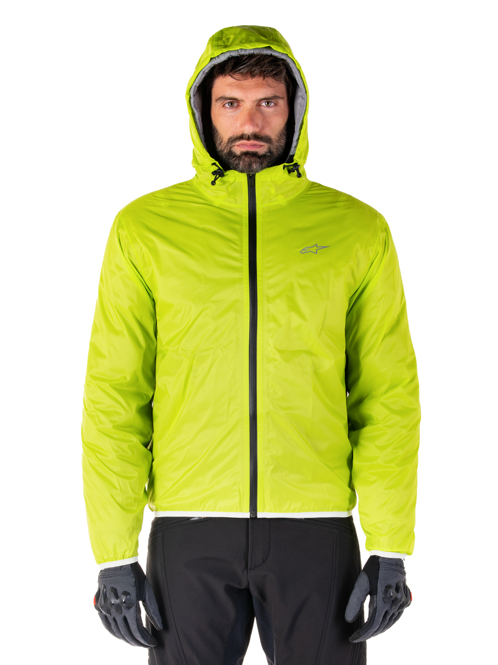 Alpinestars Mohobbs Wasserdichte Jacke, verstaubarer Regenschutz in Lime Punch, hell neongrüne Kapuzenjacke kombiniert mit schwarzer Motorradhose und grauen Motorradhandschuhen, urbaner Moto-Streetwear-Stil.