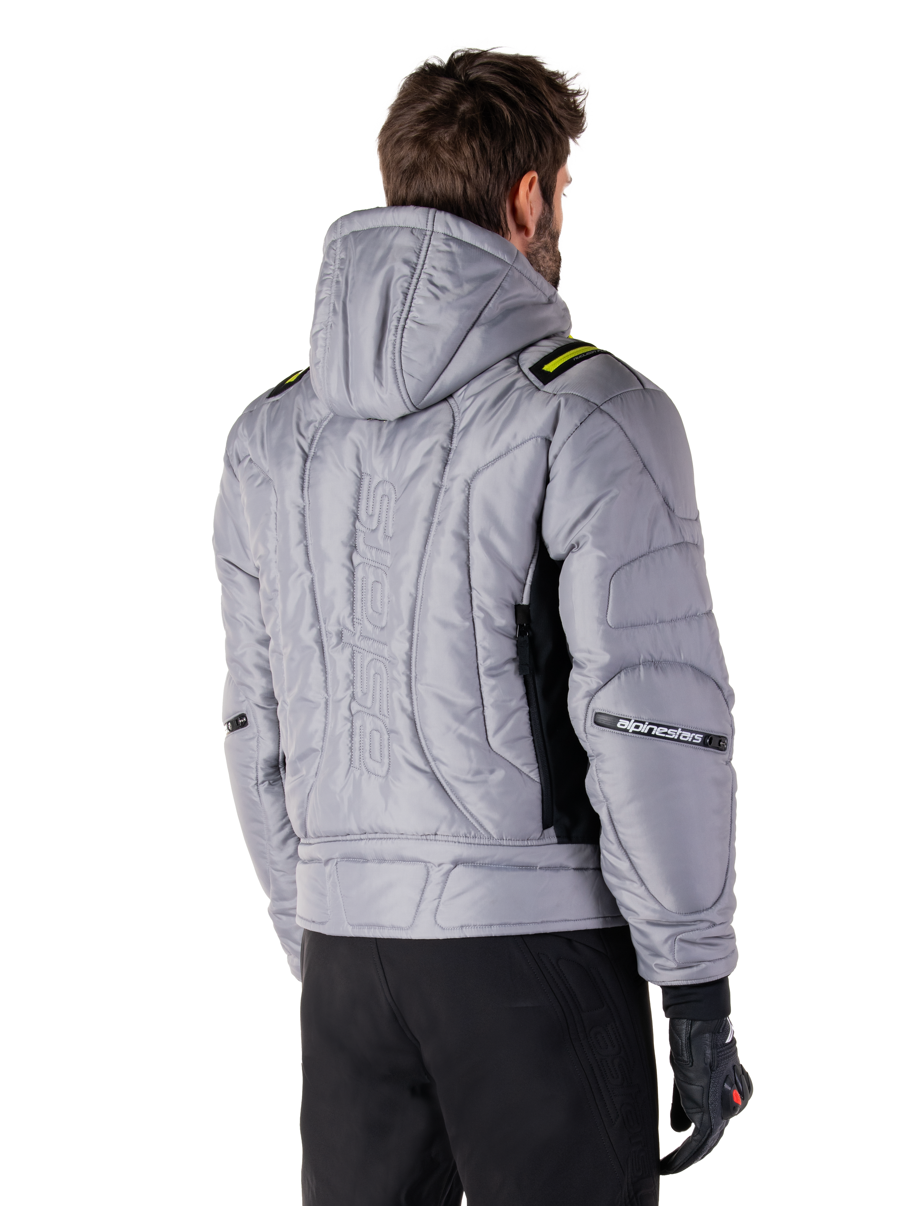 Alpinestars Mohobbs Wasserdichte Jacke in Lunar Gray und Lime Punch, Rückansicht an einem Model, gestepptes wattiertes Bomber-Design mit vertikal geprägtem Astars-Branding auf dem Rücken, limettengrüne Schulterakzente, mit Kapuze, getragen mit schwarzer Motorradhose und Handschuhen.