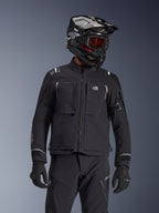 Adventure-Fahrer mit der Alpinestars Andes Pro Drystar® XF Jacke in Schwarz und Dunkelgrau, All-Terra-Branding auf der Brust, kombiniert mit passender technischer Hose und schwarzem Adventure-Helm mit Schutzbrille, professionelles Touren-Outfit.