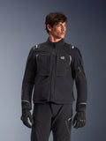 Alpinestars Andes Pro Drystar® XF Jacke, schwarz-dunkelgraue Motorrad-Adventure-Touringjacke, getragen mit passender Hose und Handschuhen, technische laminierte Schalenkonstruktion, ALL TERRA Logo auf der Brust, reflektierende Details, verstellbare Ärmelbündchen