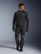 Männliches Model in Alpinestars Andes Pro Drystar® XF Jacke, Adventure-Motorradjacke in Schwarz und Dunkelgrau, kombiniert mit passender technischer Hose und Handschuhen, mit mehreren Taschen und „Terra“-Branding auf der Brust.
