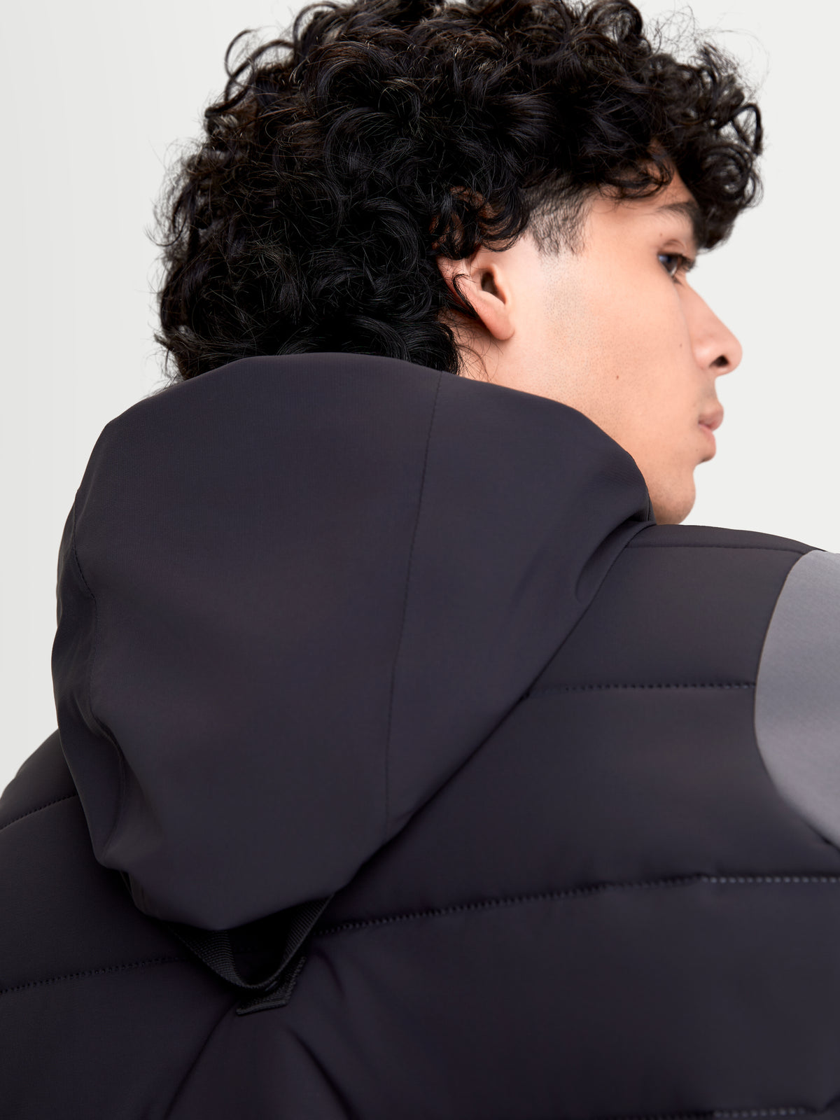 Alpinestars Therma Tech Wp Jk Motorradjacke, urbane Herren-Motorradjacke in Schwarz und Dunkelgrau, Nahaufnahme der Rückseite mit integriertem Kapuzensystem und Sonic-Welded-Down-Konstruktion an einem Model.