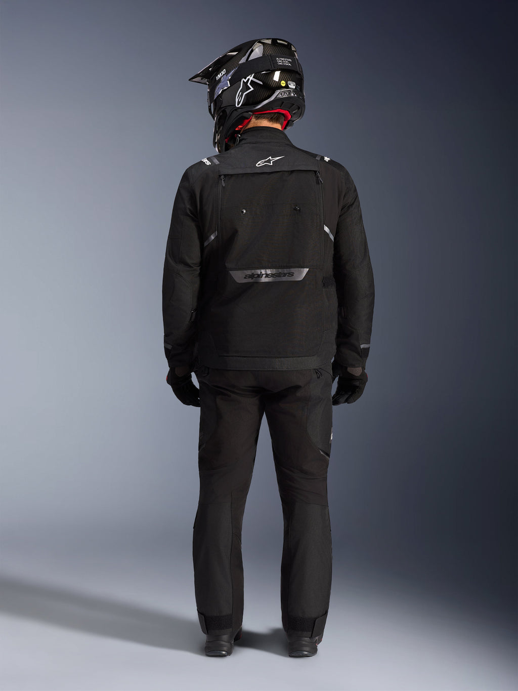 Alpinestars Cusco Drystar Jacket, Motorcycle Adventure Jacket, Black, back view worn with matching pants and a black and white helmet, featuring reflective Alpinestars branding and large ventilation panels, durable textile construction for road adventure touring