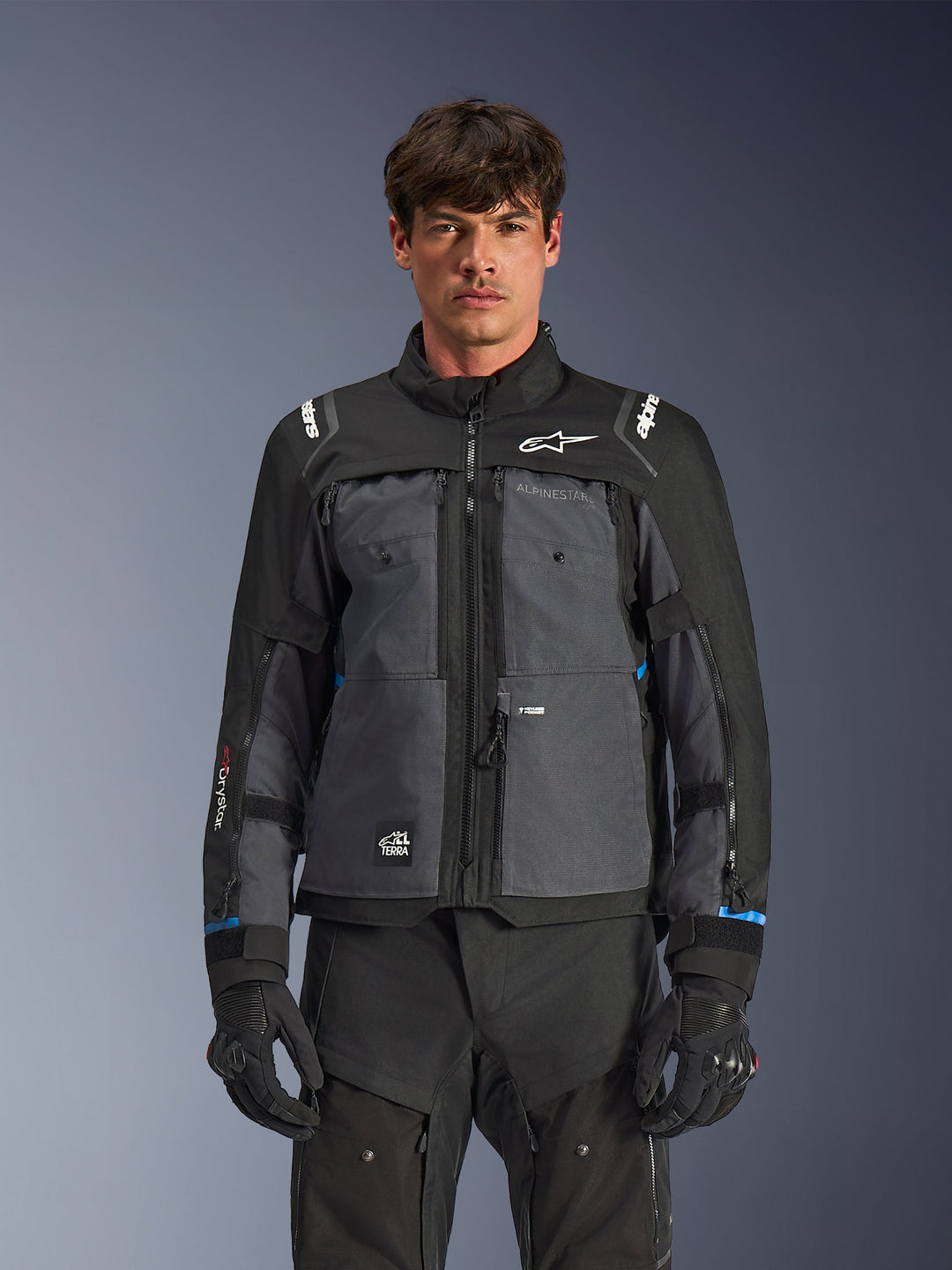Alpinestars Cusco Drystar® Jacke, Motorrad-Tourenjacke, Schwarz und Dunkelgrau, Vorderansicht am Modell, mit Alpinestars-Logos auf Brust und Schultern, Drystar®-Branding am Ärmel, technisches Multi-Pocket-Design mit Belüftungsreißverschlüssen, kombiniert mit schwarzer Motorradausrüstung