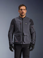 Alpinestars Maxdura Drystar®XF Laminierte Gepanzerte Schale, Adventure-Motorradjacke in Deep Gray und Schwarz, Vorderansicht am Modell, mit großen Cargotaschen, 'All Terra'-Brustlogo und Belüftungsreißverschlüssen, kombiniert mit schwarzen Motorradhandschuhen und -hosen.