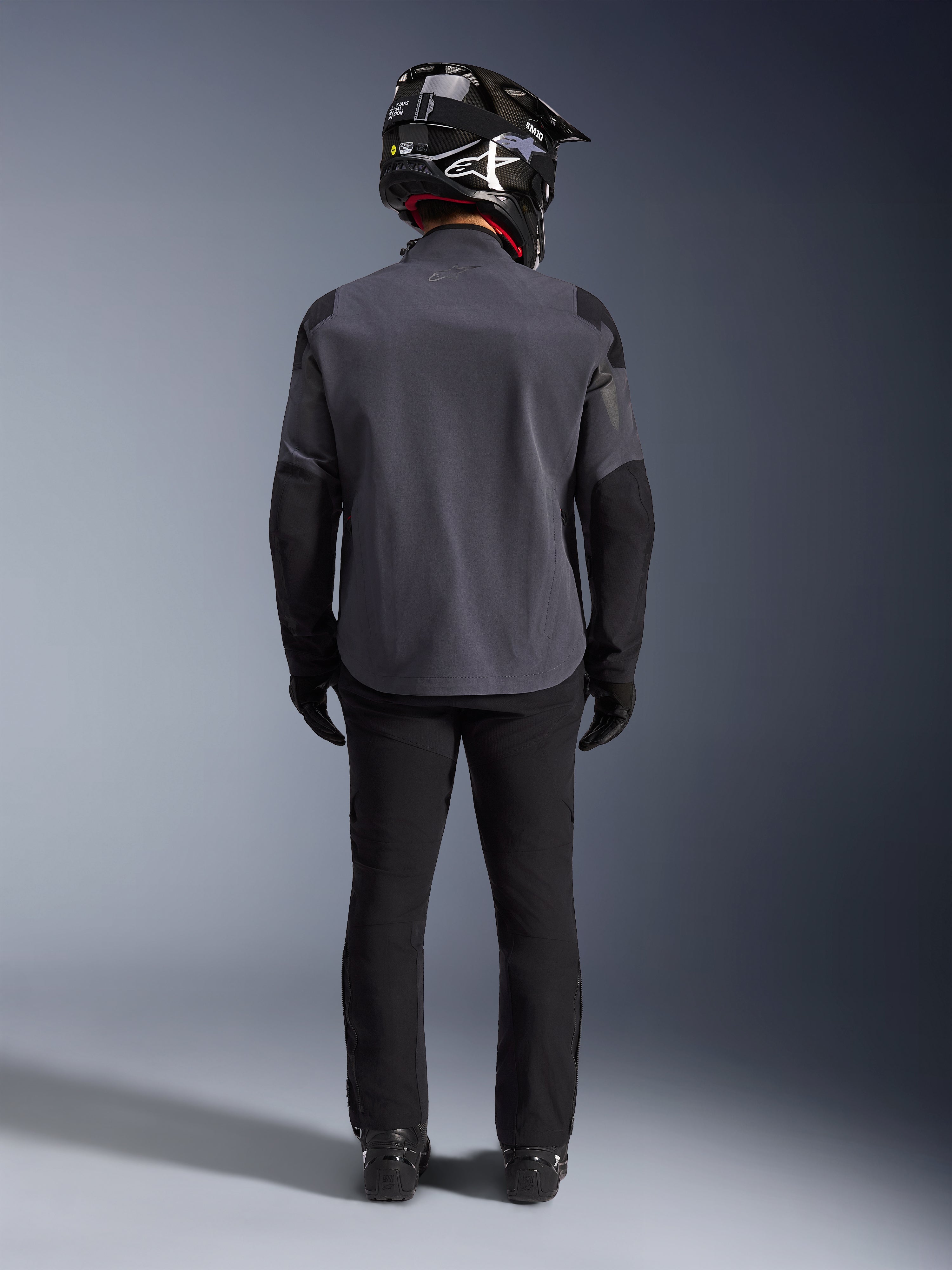 Alpinestars Maxdura Drystar®XF Laminated Armored Shell, Deep Gray Black, Ganzkörper-Rückansicht, technische Adventure-Jacke mit verstärkten Einsätzen, getragen mit schwarzer Motorradhose, Handschuhen und einem schwarz-weißen Offroad-Helm, abgestimmtes Dual-Sport-Ausrüstungsset