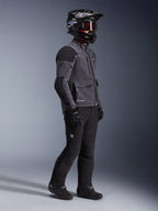 Motorradfahrer mit Alpinestars Maxdura Drystar®XF Laminated Armored Shell Jacke in Deep Gray und Schwarz, kombiniert mit schwarzer Adventure-Fahrhose, schwarzem Helm mit Brille, schwarzen Handschuhen und Stiefeln, Ganzkörper-Studioaufnahme zur Präsentation der technischen Dual-Sport-Ausrüstung.