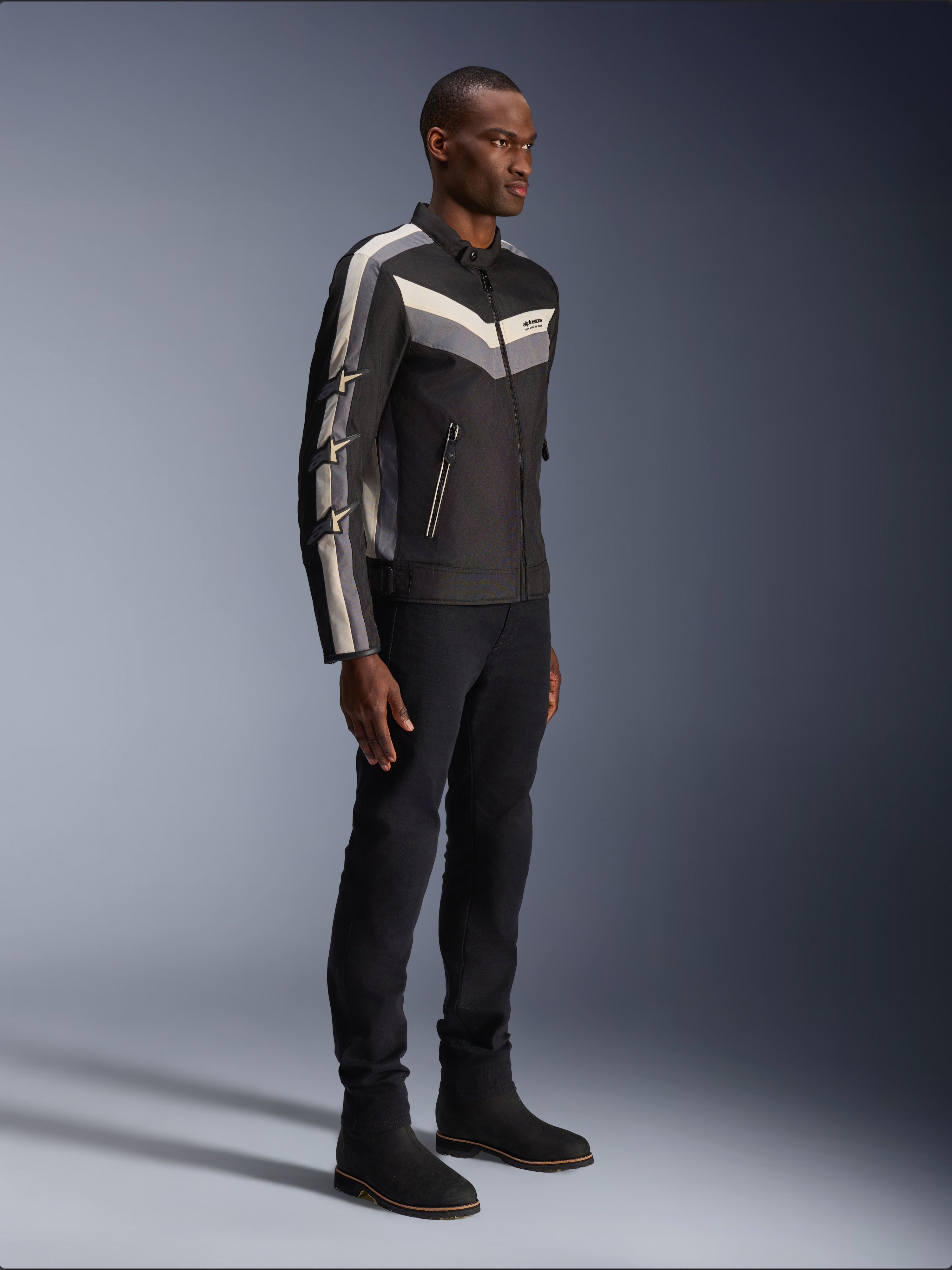 Alpinestars T-Dyno WR Jacke, Textil-Motorradjacke, Schwarz mit dunkelgrauen und ecrufarbenen Chevron-Akzenten, Vintage-inspirierte Biker-Passform, kombiniert mit schwarzer Hose und Stiefeln für einen kompletten Road-Riding-Look
