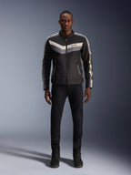Alpinestars T-Dyno WR Jacke, Schwarz, Dunkelgrau und Ecru, Textil-Motorradjacke mit Vintage-inspiriertem Chevron-Brustmuster, getragen von männlichem Model mit schwarzer Motorradhose und Stiefeln, urbane zeitgenössische Road-Ausrüstung