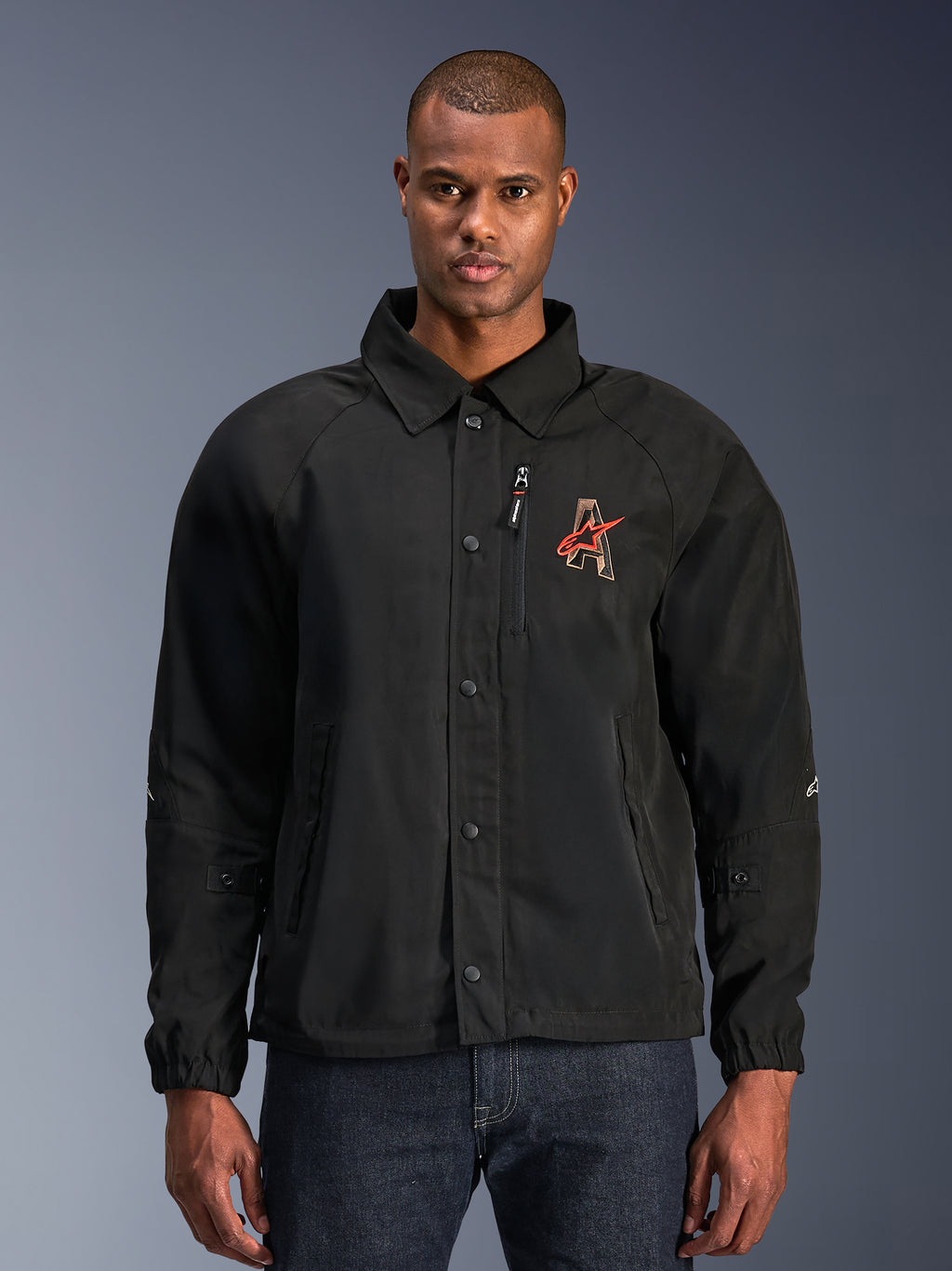 Alpinestars Revved WR Jacke, schwarze Motorradjacke mit Hemdkragen und Druckknopfleiste, rote 'A' Logo-Stickerei auf der Brust, vertikale Brusttasche mit Reißverschluss, elastische Bündchen, urbanes Coach-Jacken-Design