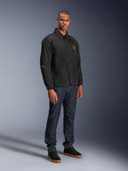 Alpinestars Revved WR Jacke in Schwarz, Motorradjacke im urbanen Coach-Stil, getragen von einem Model mit dunkelblauen Jeans und schwarzen Sneakern, mit Druckknopfleiste vorne und gesticktem Logo, minimalistisches und sportliches Design für Straßenfahrten