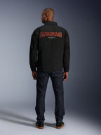 Alpinestars Revved WR Jacke, Schwarz, Rückansicht mit großer roter 'ALPINESTARS' Stickerei im 3D-Effekt, urbane Jacke im Coach-Stil, getragen mit dunkler Denim-Jeans und schwarzen Sneakern, minimalistische Motorradbekleidung