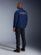 Model in der Alpinestars Revved WR Jacke in Marineblau von hinten, mit großer weiß umrandeter „ALPINESTARS“ Stickerei auf dem Rücken, kombiniert mit einer dunklen Jeanshose und schwarzen Sneakern, urbane Motorrad-Ästhetik.