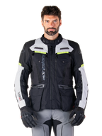 Man wearing Alpinestars Bogotá Pro Drystar® Jacket, Black Ice Gray and Yellow Fluo, all-season adventure touring motorcycle jacket, waterproof design with multiple pockets and vertical branding, paired with black gloves and gray riding pants