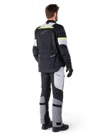 Rear view of a rider wearing the Alpinestars Bogotá Pro Drystar® Jacket in Black Ice Gray Yellow Fluo, paired with matching adventure touring pants, featuring a large back pocket and yellow fluorescent accents, all-season textile motorcycle gear.