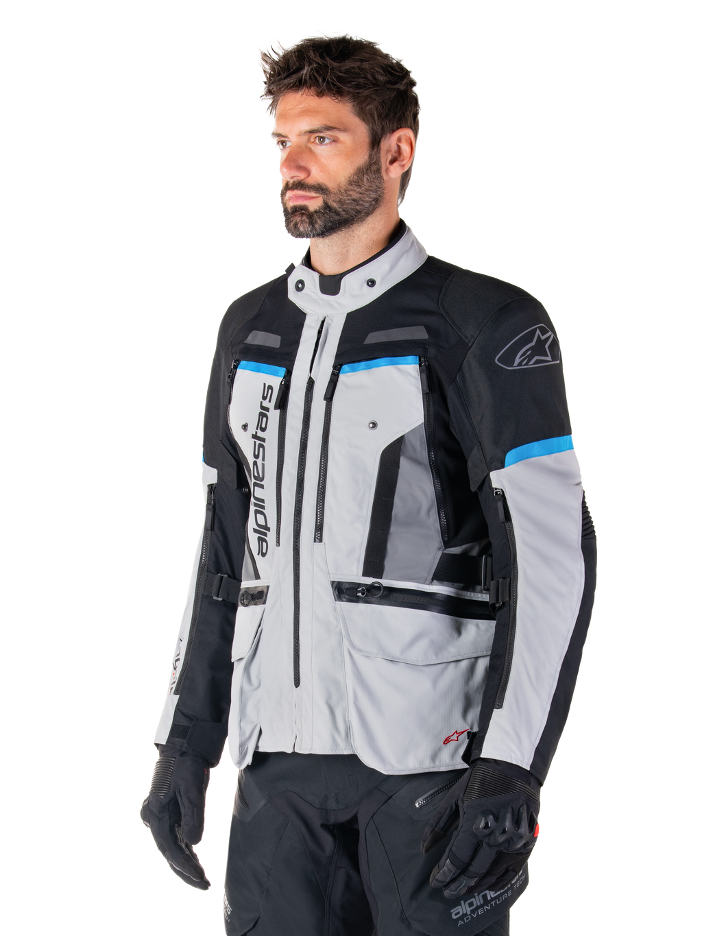 Alpinestars Bogota' Pro Drystar® Jacke, Eisgrau, Schwarz und Cyan, Adventure-Motorradjacke getragen von einem Mann mit schwarzen Handschuhen, technisches Design mit mehreren Taschen und Belüftungspanelen, Hochleistungs-Fahrerausrüstung