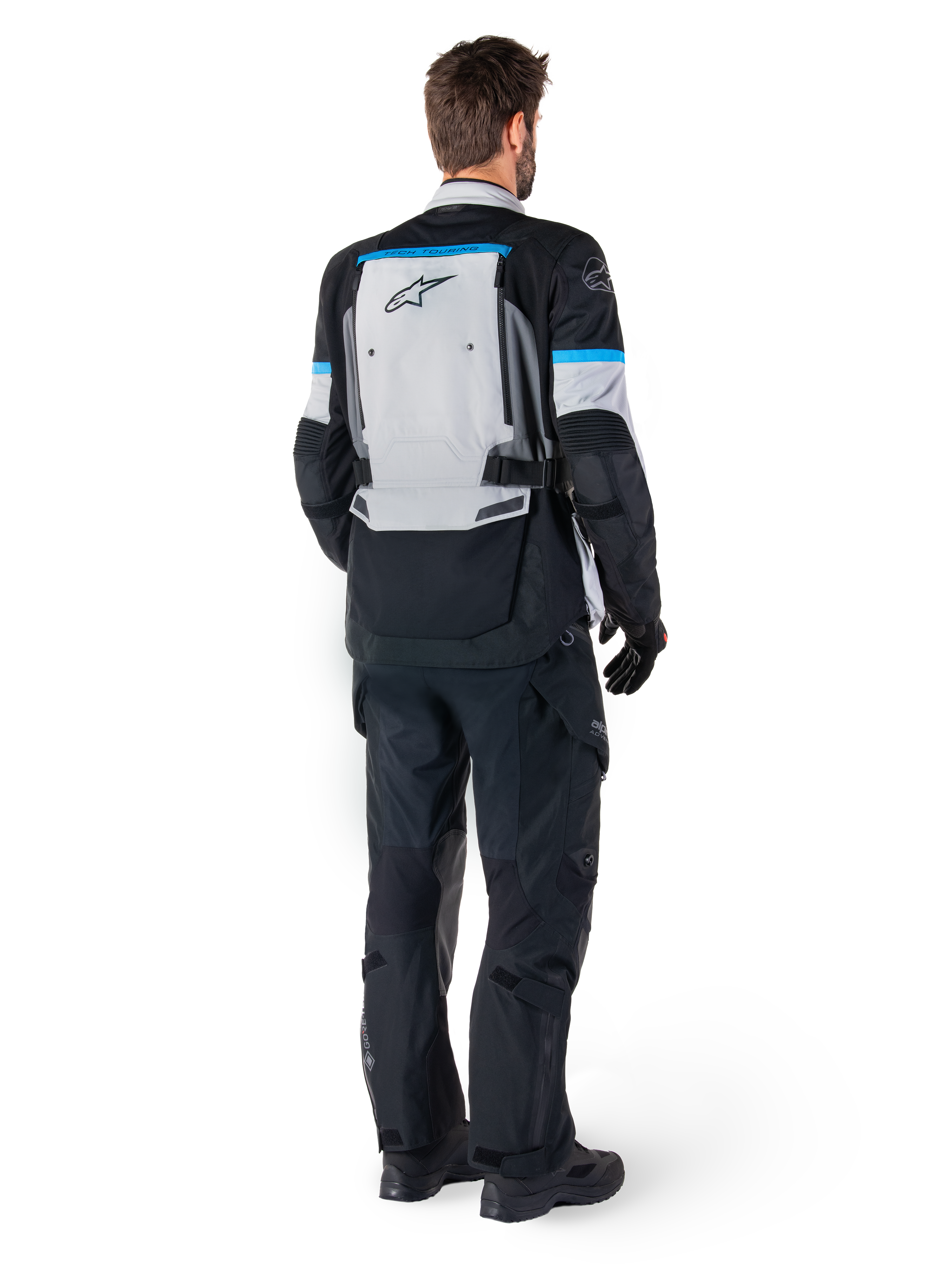 Alpinestars Bogota' Pro Drystar® Jacke, Adventure-Motorradjacke, Ice Gray, Schwarz und Cyan, Rückansicht, getragen mit passender schwarzer Hose und Handschuhen, mit einem großen grauen Rückenteil, schwarzem Alpinestars-Logo und cyanblauen Akzenten.
