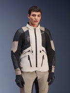 Alpinestars AMT-10LAB Drystar® XF Jacke, White Sand Aluminum Camo, Motorrad-Adventure-Jacke mit schwarzen MATRYX® Mesh-Einsätzen und Lederverstärkungen, getragen von einem Modell mit schwarzen Handschuhen und passender sandfarbener Hose, Studioporträt