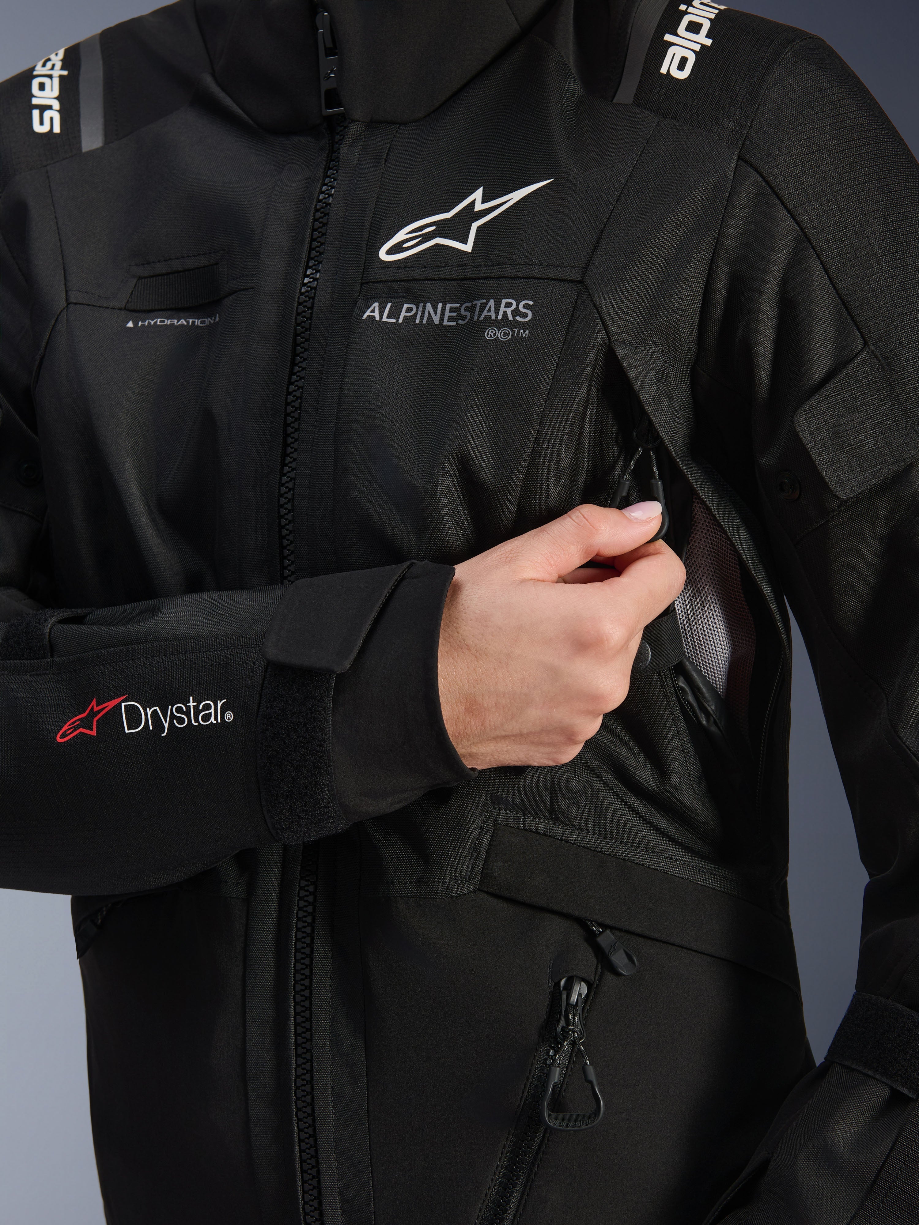 Alpinestars Damen Stella Andes V4 Drystar® Jacke, Schwarz, Detailaufnahme der geöffneten Belüftungsöffnung an der Brust, zeigt Mesh-Futter, Drystar®-Logo am Unterarm und Schlaufe für den Trinkschlauch, technische Motorradbekleidung
