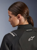 Alpinestars Stella Andes V4 Drystar® Damenjacke, Schwarz, Nahaufnahme des oberen Rückens und der Schulter, mit weiß gesticktem Astar-Logo und Branding, technische Textilkonstruktion für Motorrad-Abenteuerfahrten