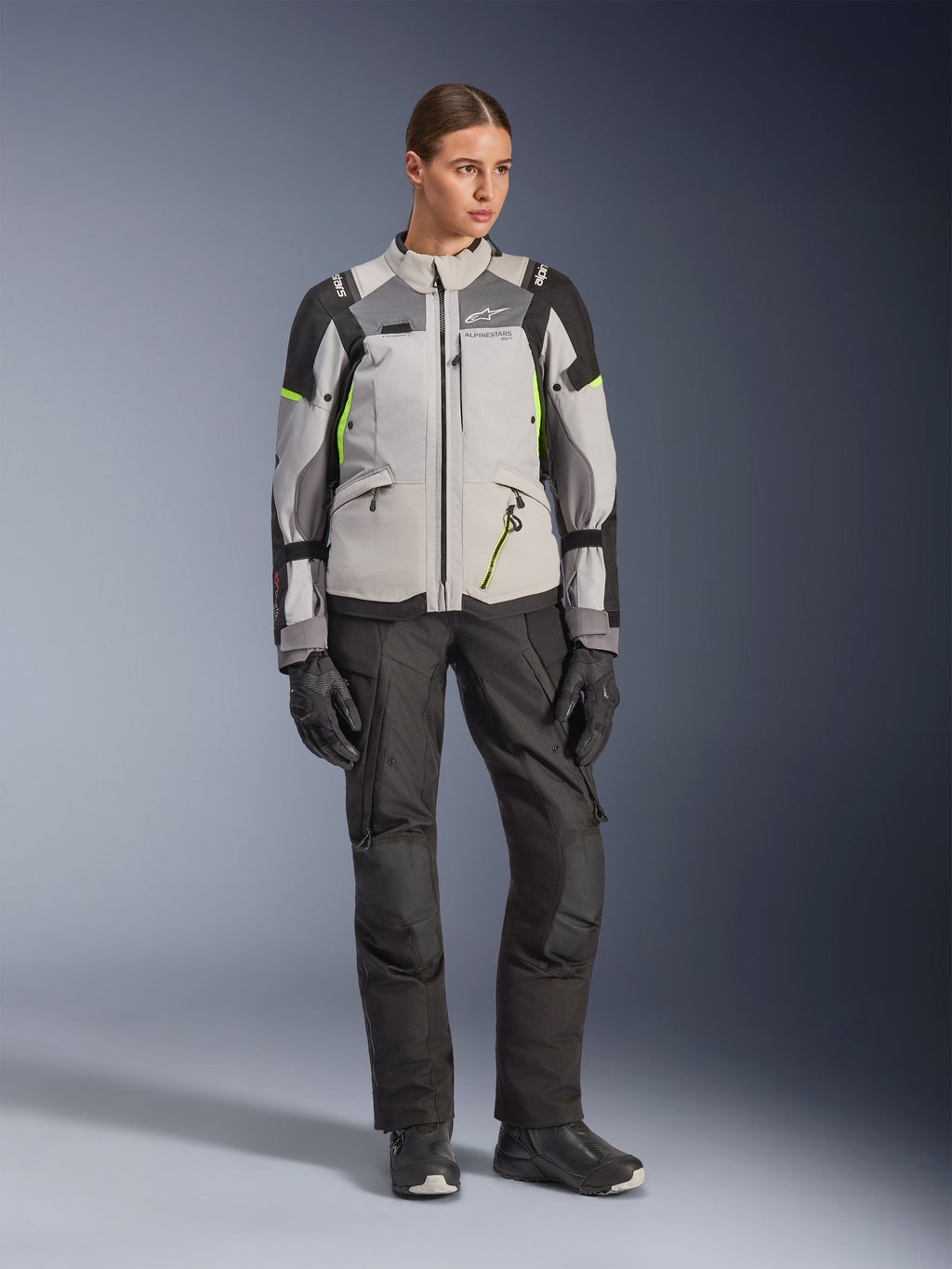 Alpinestars Stella Andes V4 Drystar® Jacke für Damen, Ice Gray, Dunkelgrau und Schwarz mit neongelben Akzenten, kombiniert mit schwarzer Motorradhose und Handschuhen, Ganzkörper-Studioaufnahme von Adventure-Tourenbekleidung.