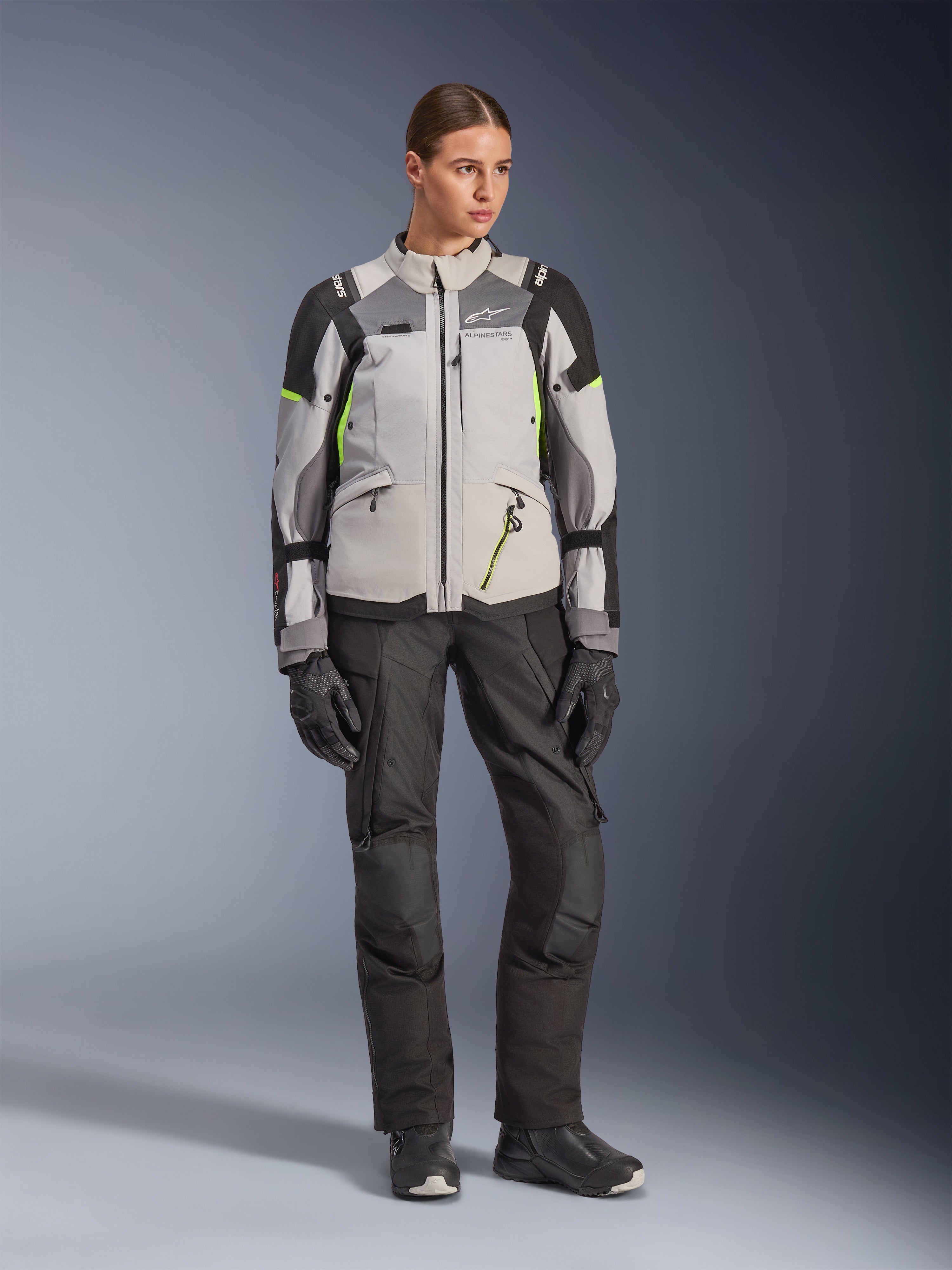 Alpinestars Stella Andes V4 Drystar® Jacke für Damen, Ice Gray, Dunkelgrau und Schwarz mit neongelben Akzenten, kombiniert mit schwarzer Motorradhose und Handschuhen, Ganzkörper-Studioaufnahme von Adventure-Tourenbekleidung.