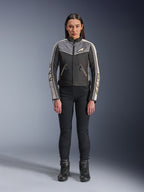Frau in Alpinestars Stella T-Dyno WR Jacke, Schwarz, Dunkelgrau und Ecru, Vorderansicht, Textil-Motorradjacke mit vintage-inspiriertem Design, Branding an Brust und Ärmeln, getragen mit schwarzer Hose und Stiefeln