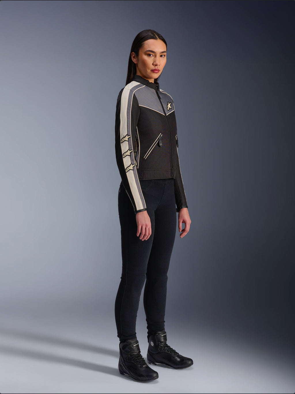 Alpinestars Stella T-Dyno WR Jacke, Textil-Motorradjacke für Damen, Schwarz, Dunkelgrau und Ecru, Vintage-inspiriertes Design mit cremefarbenen Ärmelstreifen und Stern-Logos, getragen mit schwarzer Hose und Motorradstiefeln, Heritage-inspirierte Urban-Riding-Ausrüstung