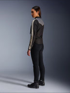Weibliches Model in der Seiten- und Rückansicht, trägt die Alpinestars Stella T-Dyno WR Jacke in Schwarz Dunkelgrau Ecru, mit vintage-inspiriertem Design, ecrufarbenen Ärmelstreifen und grauer Rückenpartie, kombiniert mit schwarzer Hose und schwarzen Motorradschuhen.