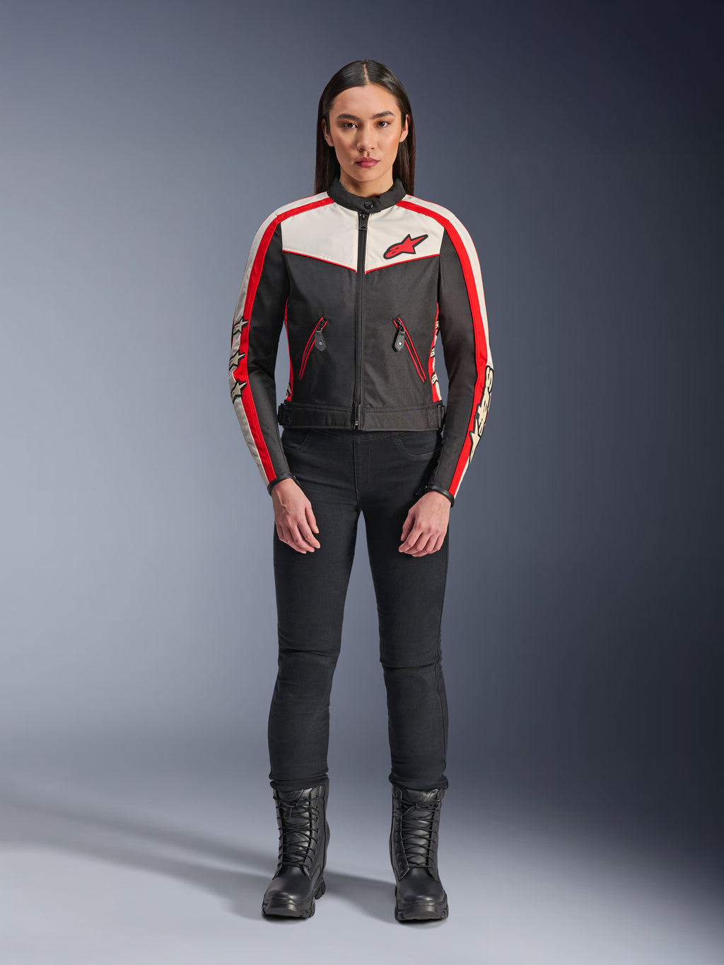 Alpinestars Stella T-Dyno WR Jacke, Textil-Motorradjacke für Damen, Schwarz, Ecru und Bright Red, getragen von einem Model mit schwarzer Hose und Stiefeln, mit Vintage-inspiriertem Design, rotem Alpinestars-Logo und Kontrasteinsätzen.
