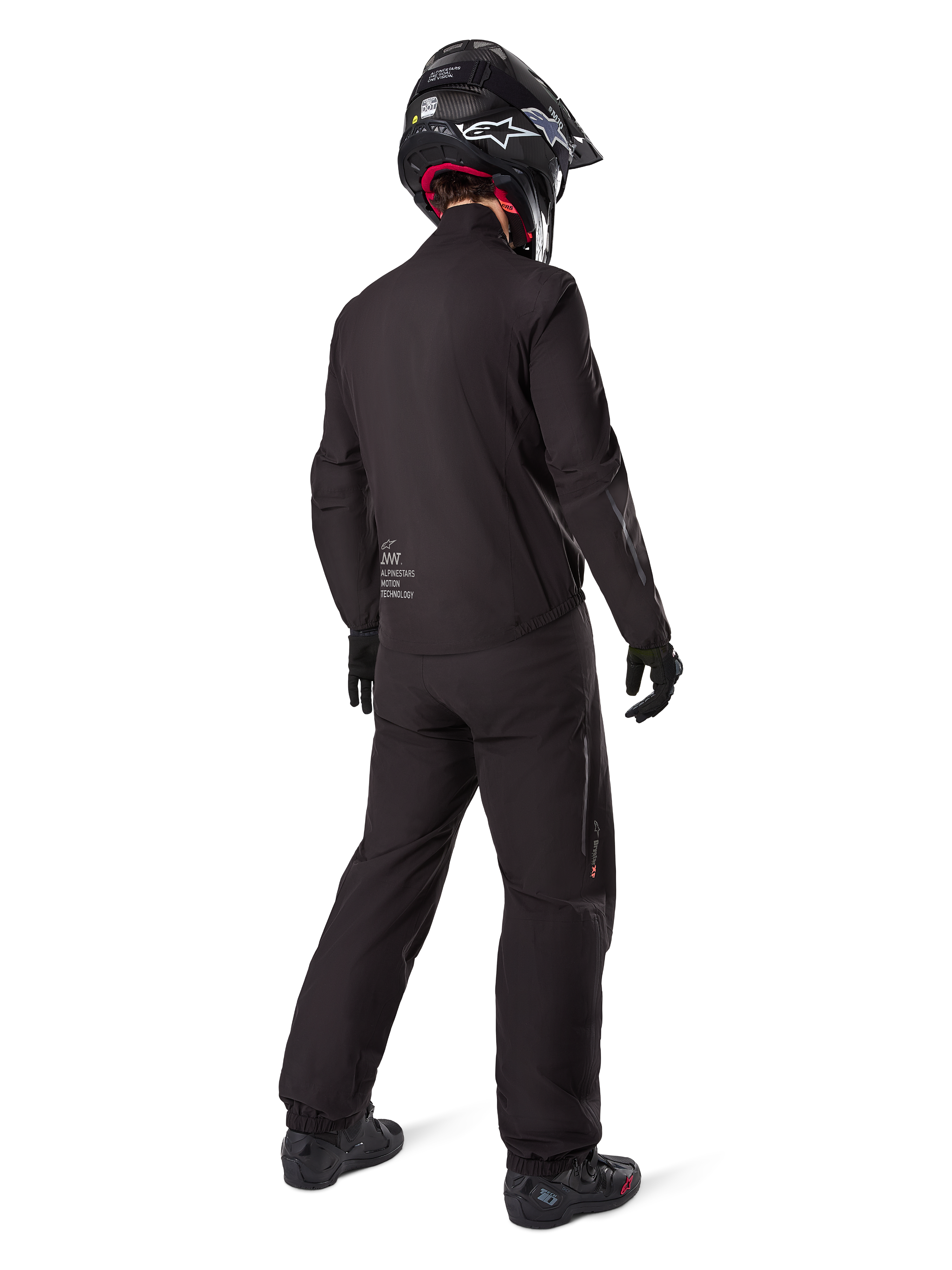 Rider from behind wearing Alpinestars Amt 8 Stretch Drystar® XF liner and pants, all-black technical adventure gear, waterproof and windproof stretch material, matching jacket with 'AMT' branding, black helmet, and boots for a complete all-weather motorcycle touring outfit