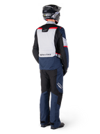 Rear view of a motorcycle rider wearing Alpinestars ST-1 Waterproof Pants and matching jacket in Dark Blue Black and Bright Red, adventure touring gear with textile panels and reflective accents, paired with a black helmet and boots.