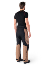 Alpinestars St-1 Waterproof Pants, motorcycle touring pants, Dark Khaki Sand and Black with Red Fluo accents, rear view on a model, featuring durable textile panels, Alpinestars logo on the thigh, and adjustable ankle cuffs, designed for all-weather adventure riding.