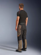 Alpinestars Cusco Drystar® Pants, Adventure Motorcycle Pants, Walnut Black, rear three-quarter view worn with a black base layer and boots, featuring reinforced textile panels, zippered cargo pockets on the thighs, and an ergonomic touring fit.