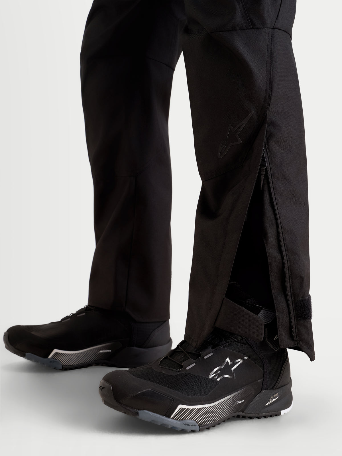 Alpinestars Stella C 1 Waterproof Hose, urbane Damen-Motorradhose in Schwarz, Nahaufnahme der erweiterten Beinausschnitte mit Reißverschluss-Einsätzen über Motorradschuhen.