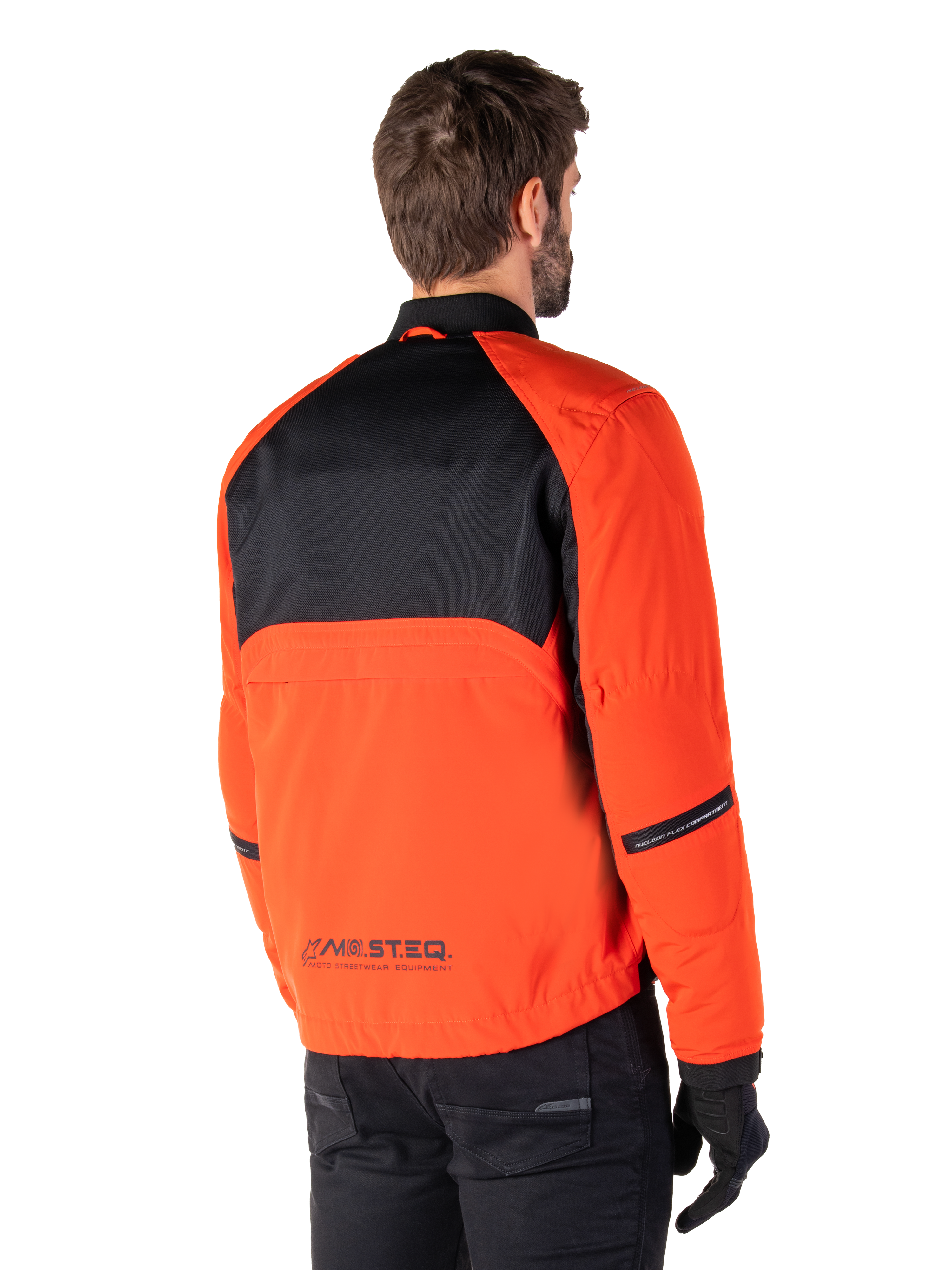 Rear view of a rider wearing the Alpinestars Mootant Waterproof Parka in Spicy Orange and Black, featuring a black mesh upper back panel and reflective MO.ST.EQ. branding, modern utilitarian motorcycle jacket.