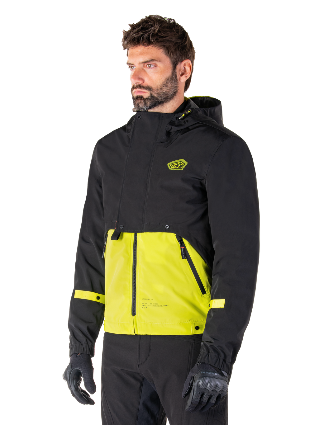 Alpinestars Mootant Waterproof Parka in Lime Punch Black, modular motorcycle jacket worn by a man with black riding gloves and pants, featuring a black upper section and sleeves with a vibrant lime green lower panel, hooded design with a utilitarian military-inspired aesthetic.