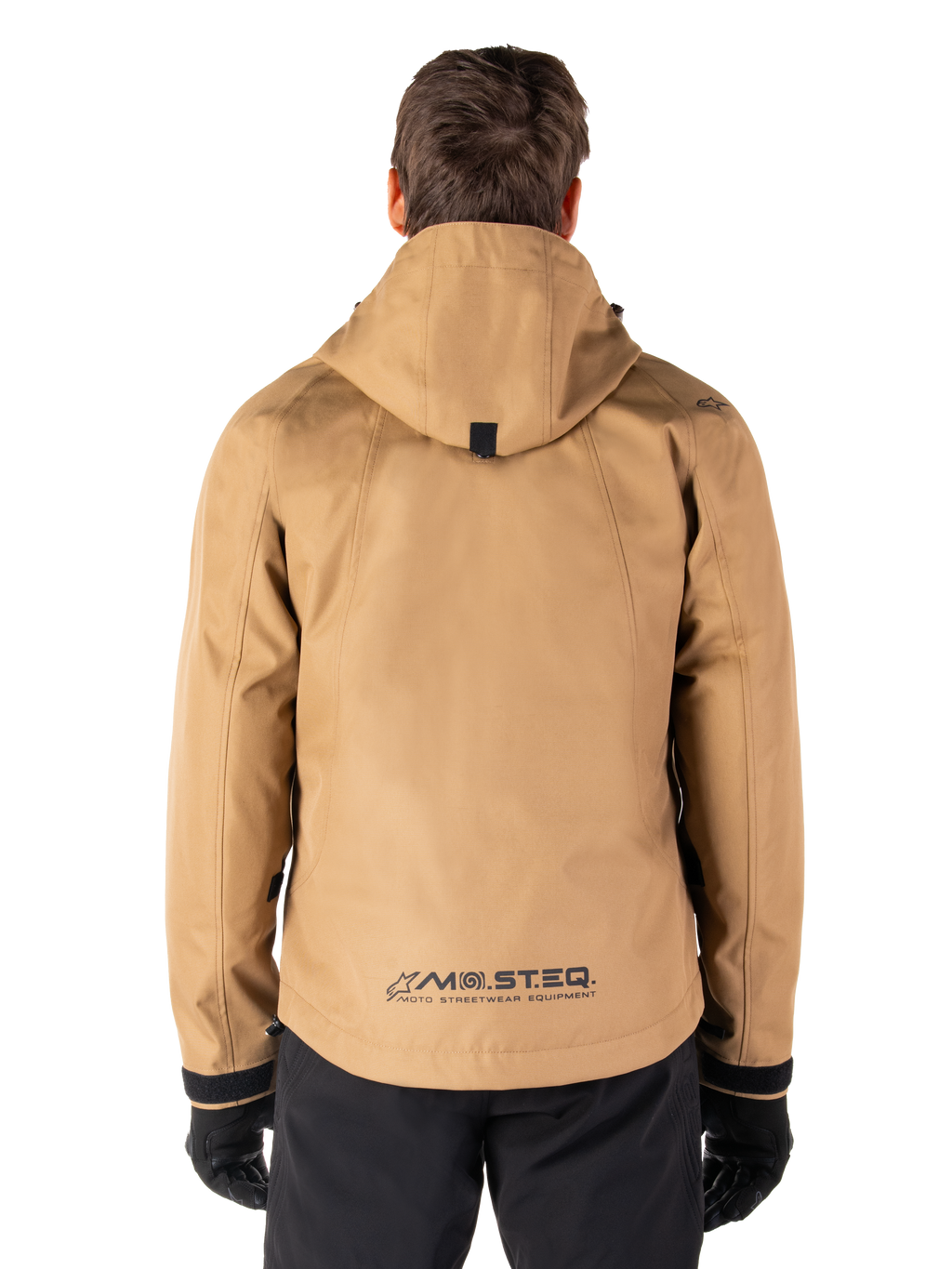Alpinestars Morush Wasserdichter Parka, Utility Brown, Rückansicht, mit Kapuze und MO.ST.EQ.-Branding am unteren Rücken, kombiniert mit schwarzer Hose und Handschuhen, moderne von Streetwear inspirierte Motorradbekleidung