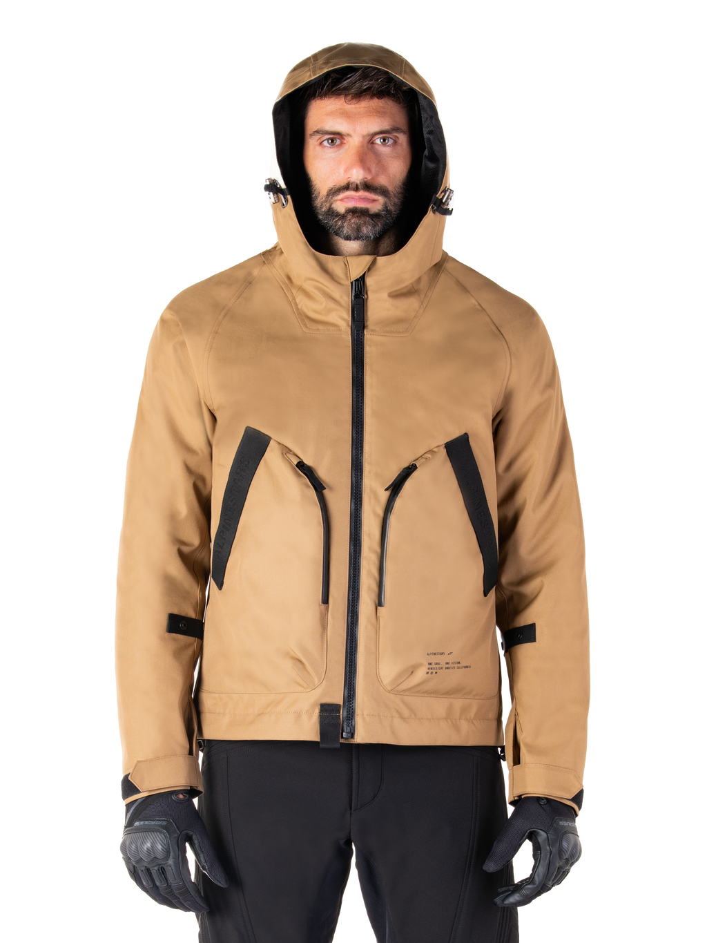Alpinestars Morush Wasserdichter Parka, Motorradjacke, Utility Brown, Kapuzendesign im Streetwear-Stil mit großen, schwarz akzentuierten Fronttaschen, kombiniert mit schwarzen Fahrhandschuhen und Hosen, moderne urbane Motorradausrüstung