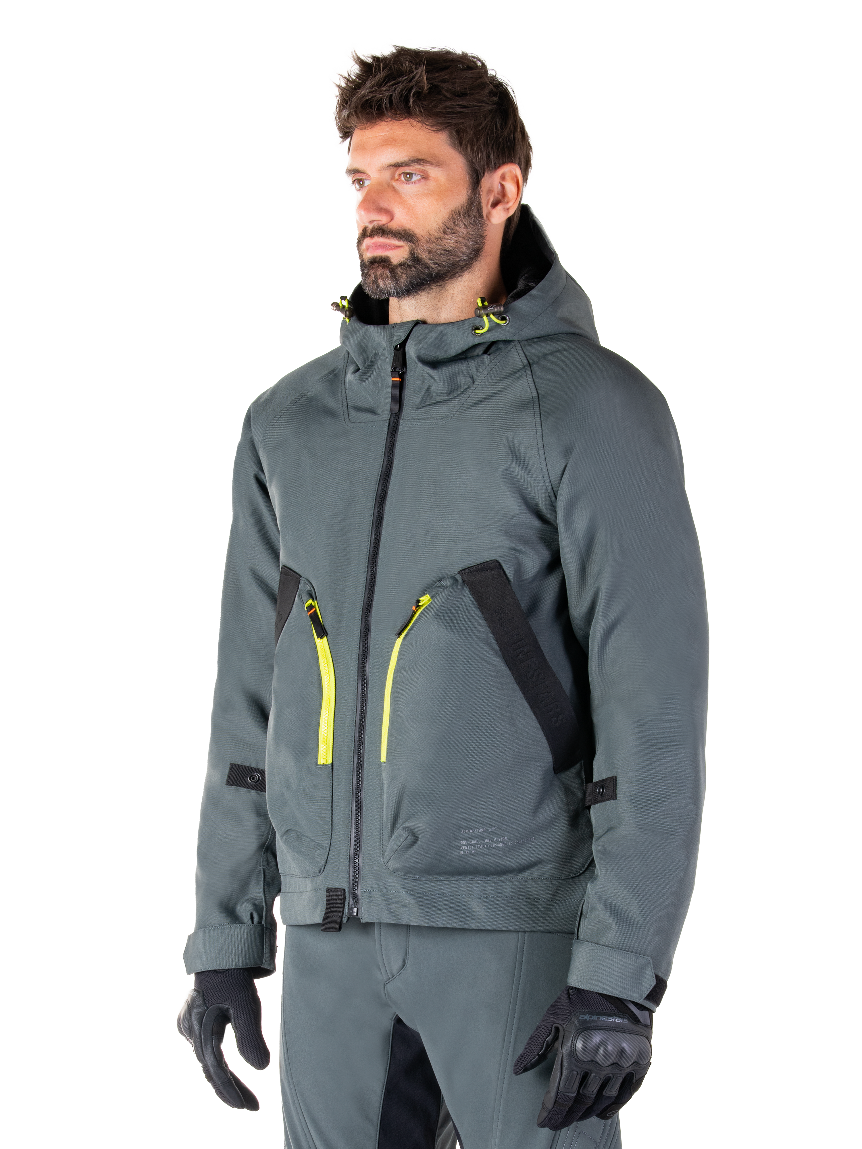 Alpinestars Morush Wasserdichter Parka, Motorradjacke in Urban Gray, Design mit Kapuze und leuchtend gelben Reißverschluss-Akzenten, schwarze Taschendetails, kombiniert mit passender grauer Motorradhose und schwarzen Handschuhen, moderne, von Streetwear inspirierte Motorradbekleidung.
