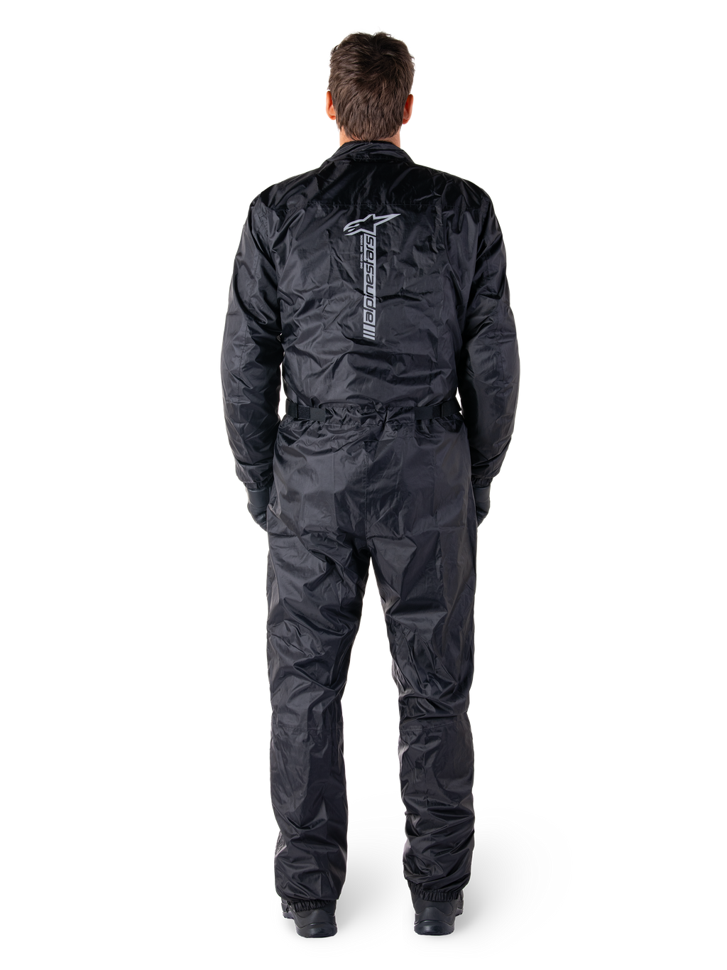 Alpinestars Hurricane Rain V2 Anzug, schwarzer einteiliger wasserdichter Motorrad-Regenanzug, Rückansicht mit großem vertikalem Alpinestars-Schriftzug und Logo, leichtes Gewebe mit elastischem Bund und Bündchen, konzipiert für Schutz bei nassem Wetter.