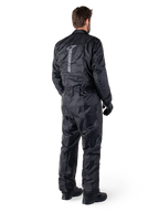Alpinestars Hurricane Rain V2 Suit, schwarzer einteiliger wasserdichter Motorrad-Regenanzug, Rückansicht mit großem vertikalem reflektierendem Logo, leichtes windabweisendes Gewebe, getragen mit schwarzen Handschuhen und Stiefeln