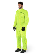 Alpinestars Hurricane Rain V2 Anzug, einteiliger wasserdichter Motorrad-Regenanzug, Gelb Fluo, getragen mit schwarzen Handschuhen und Stiefeln, mit schwarzem Alpinestars-Logo auf der Brust und reflektierenden Details an den Beinen